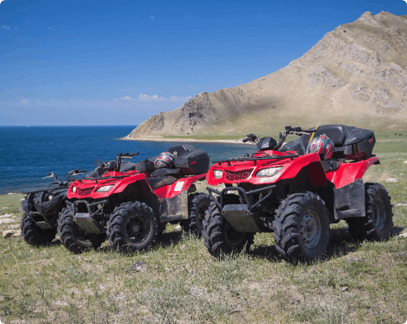 Two ATVs parked on a hill with the ocean in the background.