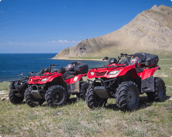 Two ATVs parked on a hill with the ocean in the background.