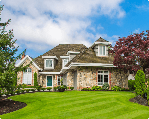 A large home surrounded by green grass and thriving plants.