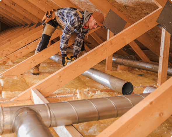 A worker installing an air duct system in an insulated home attic.