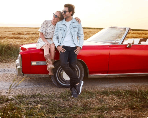 A couple sitting on their car parked in an open field.